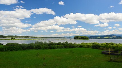 Fototapeta na wymiar Beautiful summer landscape on Orava river dam, northern Slovakia. Lawn with football goalmouth and shoreline bushes in front, Slanica Island Of Art visible in the center of dam.