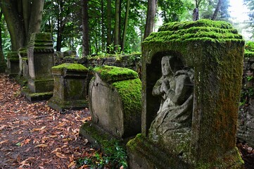 Ancient moss covered remains of cemetery gravestones, one in front with scuplture of praying...