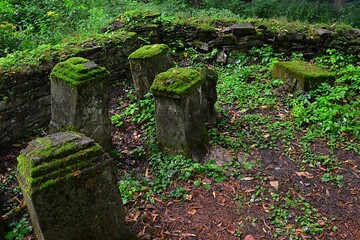 Old moss covered remains of gravestones outgrowing with plants in corner of ancient church...