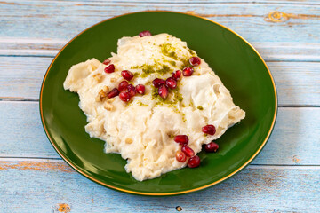 Gullac dessert on wooden background. Traditional Ramadan dessert. Güllaç dessert decorated with pistachio and pomegranate. Turkish cuisine delicacies. Close up