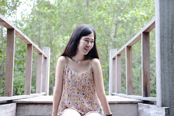 Pretty Asain girl is smiling and sitting on wooden bridge in the tropical mangrove forest at Thailand