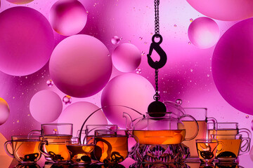 transparent glass teapot and cups with tea and drops on colorful background 