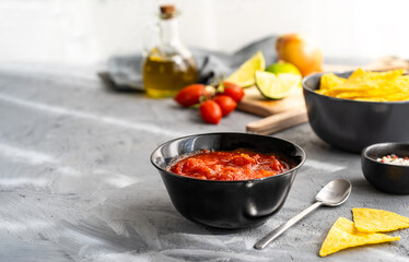 Tomato dip with nachos tortilla in bowl and basic ingredients aside