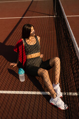 Sport lifestyle. Sport girl with bottle of water and towel. Asian model sitting on the tennis court.