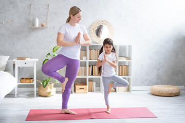 Obraz premium Young mother and little daughter in sportswear doing yoga on fitness mat at home 
