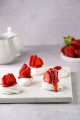 Mini-pavlova with fresh strawberries and red jam - delicious meringue cakes on marble board on off-white background