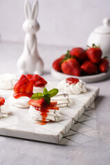 Mini-pavlova with fresh strawberries and red jam - delicious meringue cakes on marble board on...