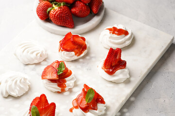 Mini-pavlova with fresh strawberries and red jam - delicious meringue cakes on marble board on off-white background