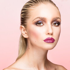 Fototapeta premium Closeup portrait of young woman with beautiful makeup and hair straightened and caught in the back, pink background.