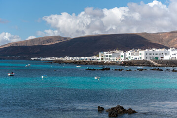 Casas blancas en Punta Mujeres en Lanzarote, Isla Canarias. Costa canaria con el mar azul turquesa y volcanes en el fondo. paisaje de la isla. 
