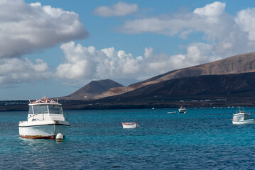 Fototapeta na wymiar mar azul claro en calma con barcos blancos y montañas volcánicas en la parte trasera de las islas canarias de Lanzarote