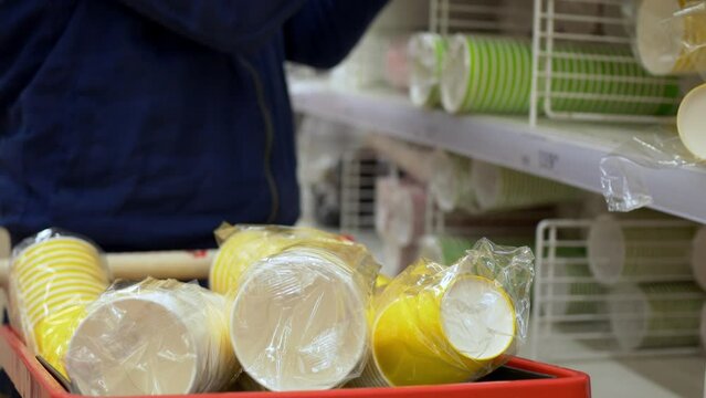 Close-up of disposable cups stacked in a shopping cart for a party or birthday. Preparing for a student party in the store, they collect a lot of paper cups for drinking on a holiday.