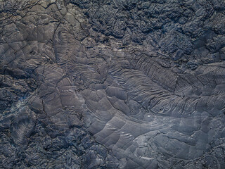Top view of solidified lava. Dark colored structures from lava flow. Pattern of deferred and broken...