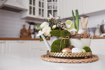An iron pot with Easter eggs, flowers and rabbits on the table.In the background is a white Scandinavian-style kitchen. The concept of home comfort and decor in the bright holiday of Easter 2022.