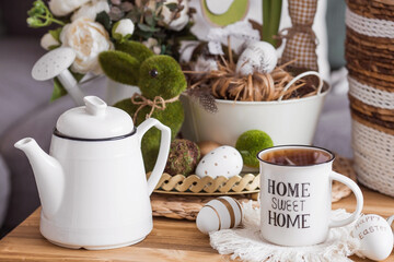 Easter morning. White-green colors. Iron vases with Easter eggs, flowers, a rabbit, a teapot and a cup in the interior of the living room. The concept of home comfort in the bright holiday of Easter.