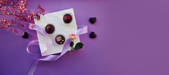 Purple chocolate background candies top view with shadows and gypsophila. Extra wide banner.