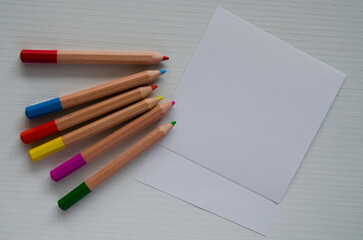 Small colored pencils and sheets of white paper on the table, top view. Template, a place for drawing,writing,sketches.