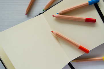 Colored pencils and an open notebook, top view. An empty space for writing, sketches.