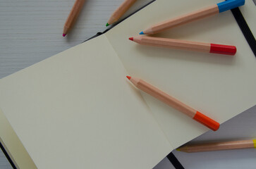 Colored pencils and an open notebook, top view. An empty space for writing, sketches.