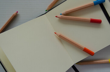 Colored pencils and an open notebook, top view. An empty space for writing, sketches.