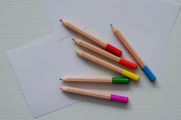 Small colored pencils and sheets of white paper on the table, top view. A template, a place for drawing,writing,sketches.