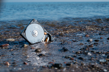 computer hard disk lies in the shore sand of the sea and is washed by the water