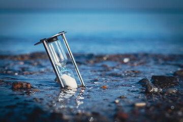 hourglass is stuck in the shore sand of the sea and is washed around by the water