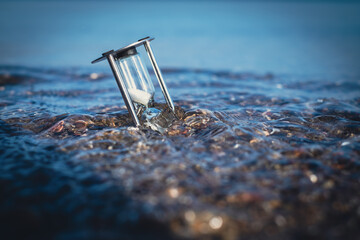 hourglass is stuck in the shore sand of the sea and is washed around by the water