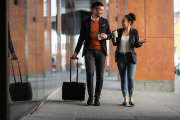 Business man and woman walking and drinking coffee. Businesspeople traveling together with luggage.