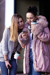 Two girl looking at phone. Friends gossiping outdoors on a cold winter day..