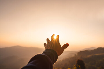 Young man hand reaching for the mountains during sunset and beautiful landscape