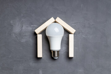 House symbol made by wooden blocks, led light bulb inside over cold cement background. above view....