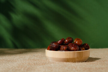 dried dates in a wooden plate on a green background on a sunny day.
