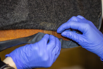 The process of tightening the car interior.Tailor's hands in blue gloves while working with fabric.Tightening of the car interior.The hands of a girl in blue gloves during work are selective focus.