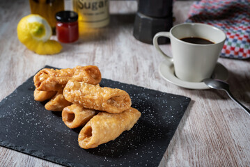 Pestiños next to a cup of coffee, with some of the ingredients used in its preparation.