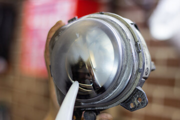 Car headlight during repair and cleaning. Perfectly smooth headlight glass. The mechanic restores the headlight of the car with the help of a chemical kettle. Restoration of automotive optics.