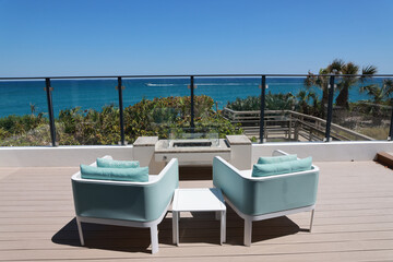 An inviting oceanfront seaside view with comfortable lounge chairs on a protected terrace.