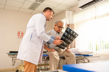 Doctor talking to senior patient at bedside in hosptial ward.Young male doctors doing analysis x-ray scan photo with senior asian elderly male patient during lying on bed in patient room at hospital.