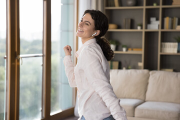Happy joyful active Latin girl with wireless earphone in ear enjoying favorite songs, tunes,...