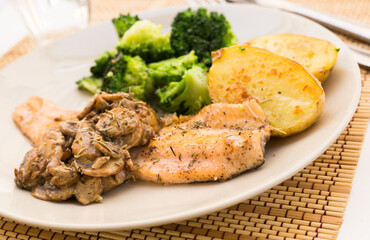 fried river trout fillet with a complex side dish of broccoli, baked potatoes and mushroom sauce