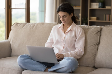 Naklejka premium Serious student girl doing research study, using laptop computer, watching online class, webinar, writing essay. Focused freelancer employee working from home, browsing Internet