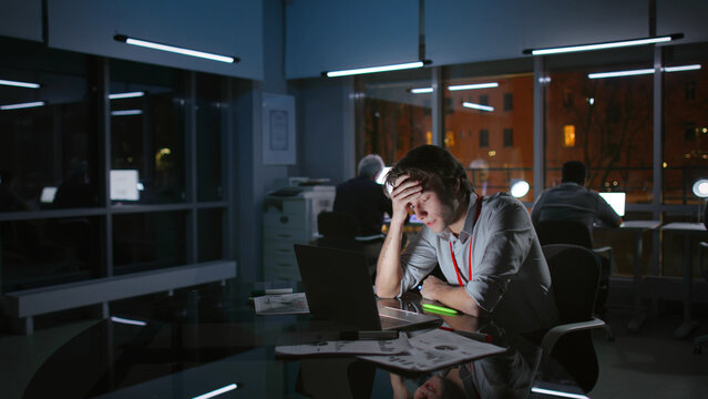 Portrait of exhausted stressed businessman work on laptop at night in dark office