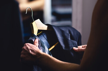 Man getting ready and dressing up in a suit. Luxury jacket and tie in hanger. Trying on outfit before date or wedding. Fitting room in mall store, closet or tailor shop. Formal businessman fashion.