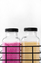 Smoothies with berries and fruits in two glass bottles in the wire basket against the white background. Healthy drink variation and kids food