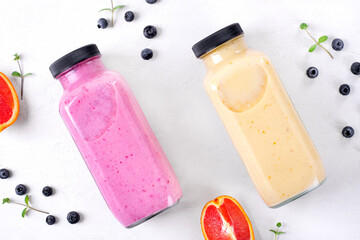 Smoothies with berries and fruits in two glass bottles on the white table. Healthy drink variation and kids food. Flat lay - 495255541