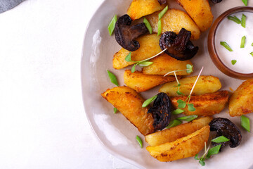 Roasted potato wedges with mushrooms and spices served with yogurt sauce topped with microgreen. Hot meal. Top view