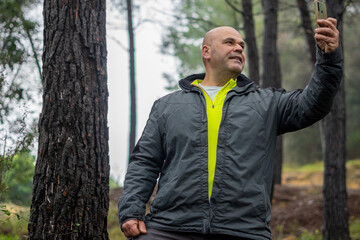 Hiker man taking a selfie with the phone, in a wet and foggy forest.