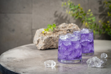 Blueberry purple drink with ice in a glass on gray stone background. A summer refreshing drink.