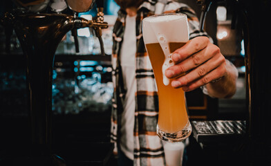 bartender's hand holds out a full glass of beer in a bar 