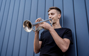 Young street musician playing the trumpet near the big blue wall © romaset
